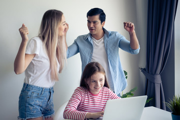 little girl using laptop computer and get winning prize, mother and father happy together at home, young happy family concept