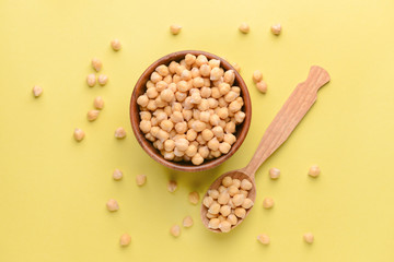 Bowl with raw chickpea and spoon on color background