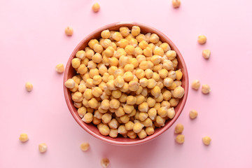Bowl with raw chickpea on color background
