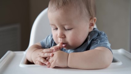 Baby playing with his feet close up on high chair. Portrait of a cute baby bites, nibbles and sucks his own feet and finger in 4k