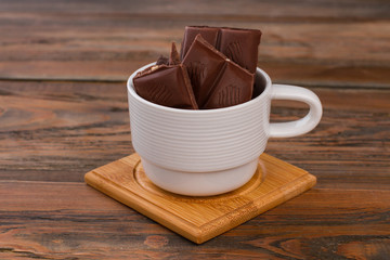 Cup with chocolate pieces on wooden background. Chocolate in white cup on wooden table. Yummy treats from natural cacao.