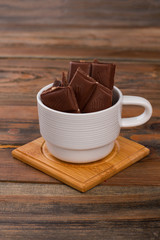 Chocolate pieces in cup on wooden background. White cup with chocolate on wooden table.