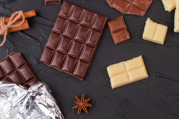 Delicious chocolate bars on black concrete background. Chocolate pieces and spices on dark background.