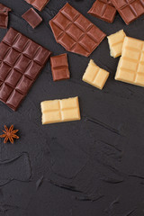 Different chocolate bars on black stone background. Various chocolate bars. Flat lay, copy space.