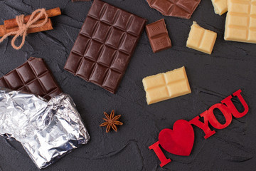 Romantic background with chocolate bars. Different chocolate pieces and inscription I love you on black background.