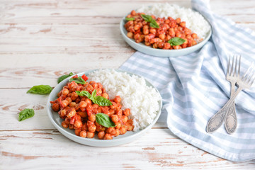 Plate with tasty chickpea in tomato sauce and boiled rice on table