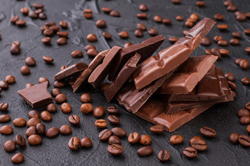 Coffee beans and broken chocolate on black background. Close up of chocolate pieces and roasted coffee beans.