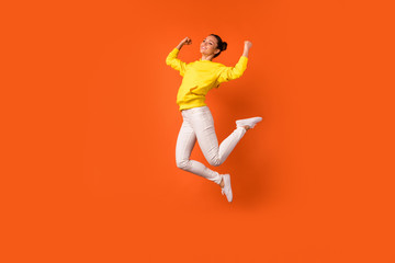 Fototapeta na wymiar Full length photo of cheerful lovely lady raise fists smiling jumping dressed white pants trousers isolated over orange background