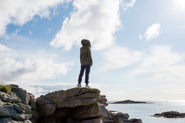 A girl stands high on stones. Success, happiness, freedom. Ocean and clouds. Beautiful nature landscape in Norway. Amazing scenic outdoors view in North. Travel, adventure, lifestyle. Lofoten Islands