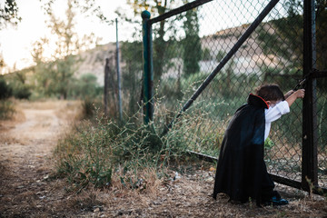 Kid costumed of dracula to halloween on the forest near grille