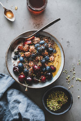 Healthy breakfast. Flat-lay of quinoa oat granola coconut yogurt bowl with fresh fruit, honey, seeds, nuts, berries over grey concrete table background, top view. Clean eating, vegetarian food concept