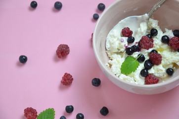 Ricotta with fresh berries and honey on pink table. Cottage cheese, curd cheese or tvorog with berries in bowl. Summer dessert, breakfast or healthy snack. jar of honey blueberries and raspberries