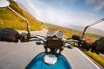 Motorcycle driver riding in Alpine highway, handlebars view, Dolomites, central Europe.