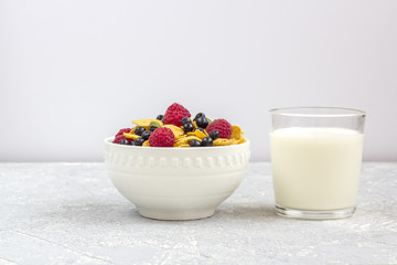 Healthy tasty breakfast: bowl with corn flakes and berries and glass of milk.