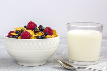 Healthy tasty breakfast: bowl with corn flakes and berries and glass of milk.