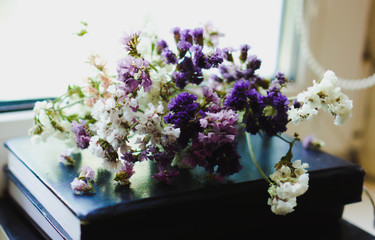 A bouquet of dried violet, pink and white wildflowers lying on the book. Bright flowers lit by sunlight. Soft selective focus, macro flowers. Photo background