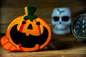 Happy Halloween Jack O Lantern halloween pumpkin with scary skull and alarm clock  on wooden background.