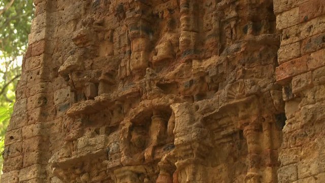 A closeup shot with downward tilting view of the facade of the Khmer ruins of Sambor Prei Kuk showing a nearly unrecognizable design figure on its brick wall exterior..