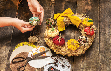 Female hands sew a textile pumpkin to decorate an autumn straw wreath on a wooden background. DIY