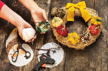 Female hands sew a textile pumpkin to decorate an autumn straw wreath on a wooden background. DIY