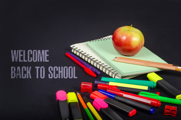 Back to school concept. Red apple on notebooks and with pencils, markers on dark background.  U