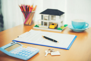 House model, calculator and house key lying on real estate contract, home loan and investment concept.