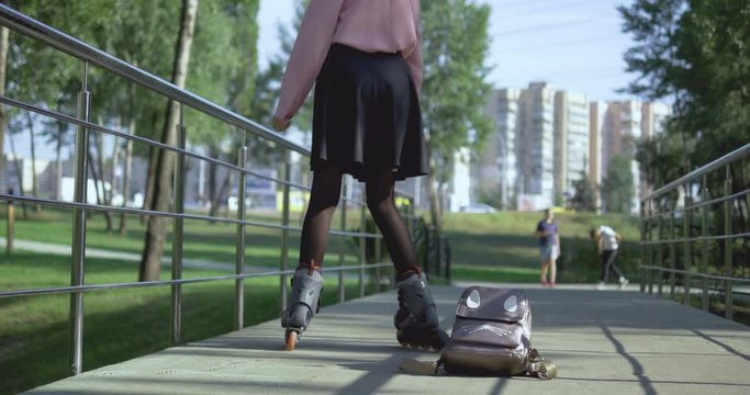 On a warm autumn day, in a school uniform with a backpack, a schoolgirl rides a bridge after school and roller-skates through a city park