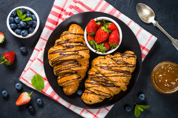 Croissant with fresh berries and cup of coffee on black.
