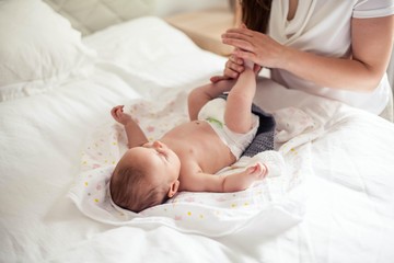 Young beautiful mother holds a baby. Mom gives the baby a massage on the bed.