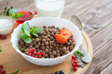 Cereal chocolate balls in bowl with milk on rustic wooden table Healthy tasty breakfast chocolate balls with strawberries, raspberries, black currants and red currants.