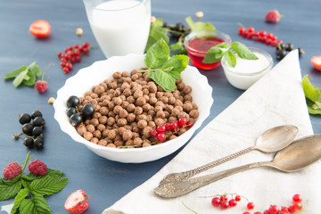 Cereal chocolate balls in bowl with milk on rustic wooden table Healthy tasty breakfast chocolate balls with strawberries, raspberries, black currants and red currants.
