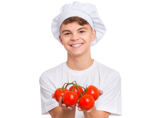 Happy teen boy in chef hat holding fresh red tomatoes branch, isolated on white background. Portrait of cute smiling child shows delicious raw vegetables in hands. Organic natural healthy food produce