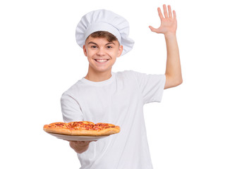 Happy handsome teen boy in chef hat holding cooked appetizing pizza. Guy holds plate with fresh pizza in his hands, isolated on white background. Portrait of cute child showing delicious Italian pizza