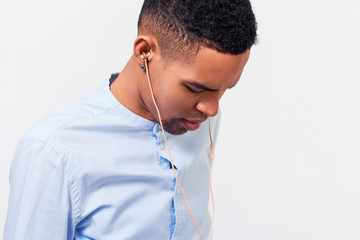 Clsoe-up portrait of dark-skinned man listening the music through earphones. Indoor shot of African American young male wears blue shirt, looking down. People, technology and music concept