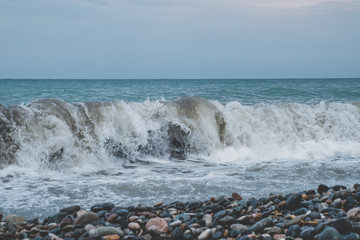Stormy waves on the sea coast on a gloomy day. Large waves of a stormy sea crash on a pebble beach.