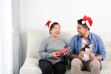 Asian senior woman mother and young man son in blue shirt give gift box for Christmas gift in living room