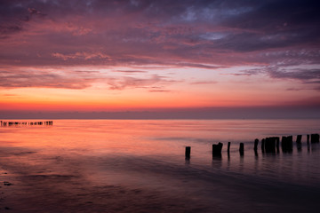 Colorful sunrise at beach of baltic sea in summer with silhouette of old poles groins, Groemitz, Schleswig-Holstein, Germany