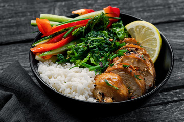 Delicious Buddha bowl with teriyaki chicken, fresh vegetables and basmati rice on a black table with dark tablemat.