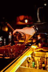 Barman pouring fresh alcoholic drink into the glasses with ice cubes on the bar counter