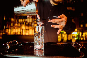 Barman pouring fresh alcoholic drink into the glasses with ice cubes on the bar counter