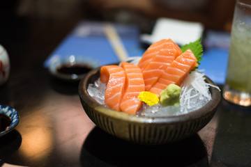 Salmon raw sashimi on brown Japanese traditional dish on black table. Closed up.