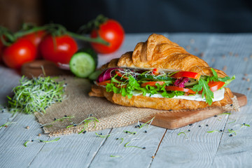 Croissant sandwiches served on wooden board. Croissants with egg, melted cheese, parsley, chicken ham, smoked salmon