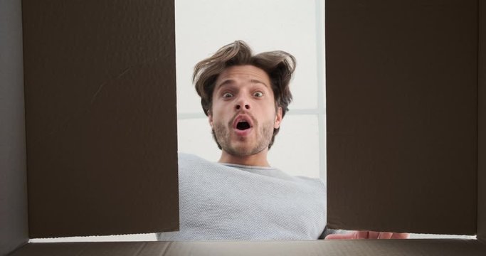 Young man surprised on unpacking a big carton box