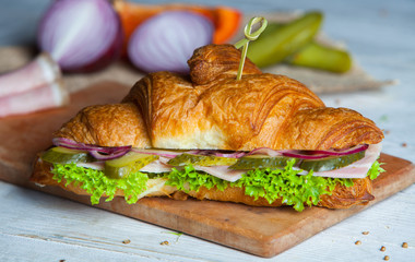 Croissant sandwiches served on wooden board. Croissants with egg, melted cheese, parsley, chicken ham, smoked salmon