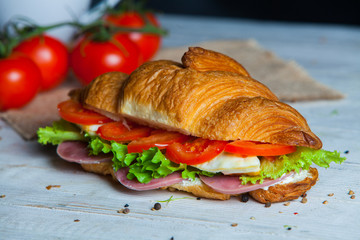 Croissant sandwiches served on wooden board. Croissants with egg, melted cheese, parsley, chicken ham, smoked salmon