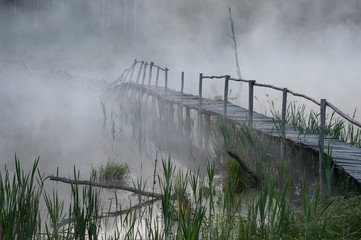 Misty bridge on the foggy lake in the morning at dawn. Cold water reflection