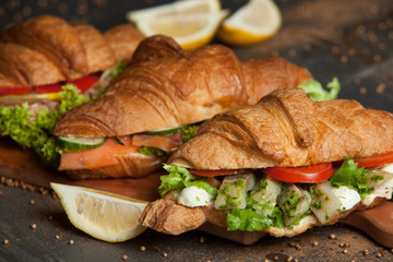 Croissant sandwiches served on wooden board. Croissants with egg, melted cheese, parsley, chicken ham, smoked salmon
