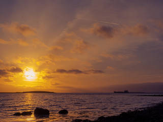 Fototapeta na wymiar Sunset over ocean surface, Cargo ship silhotte , Cloudy dramatic sky, Galway Bay, Ireland.