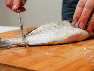 Fishmonger descaling fresh raw sea bream on a wooden cutting board with a knife, Selective focus.