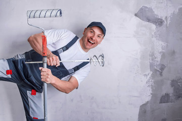 Smiling worker in overall and cap holding a nozzle for electric building mixer covered with putty...
